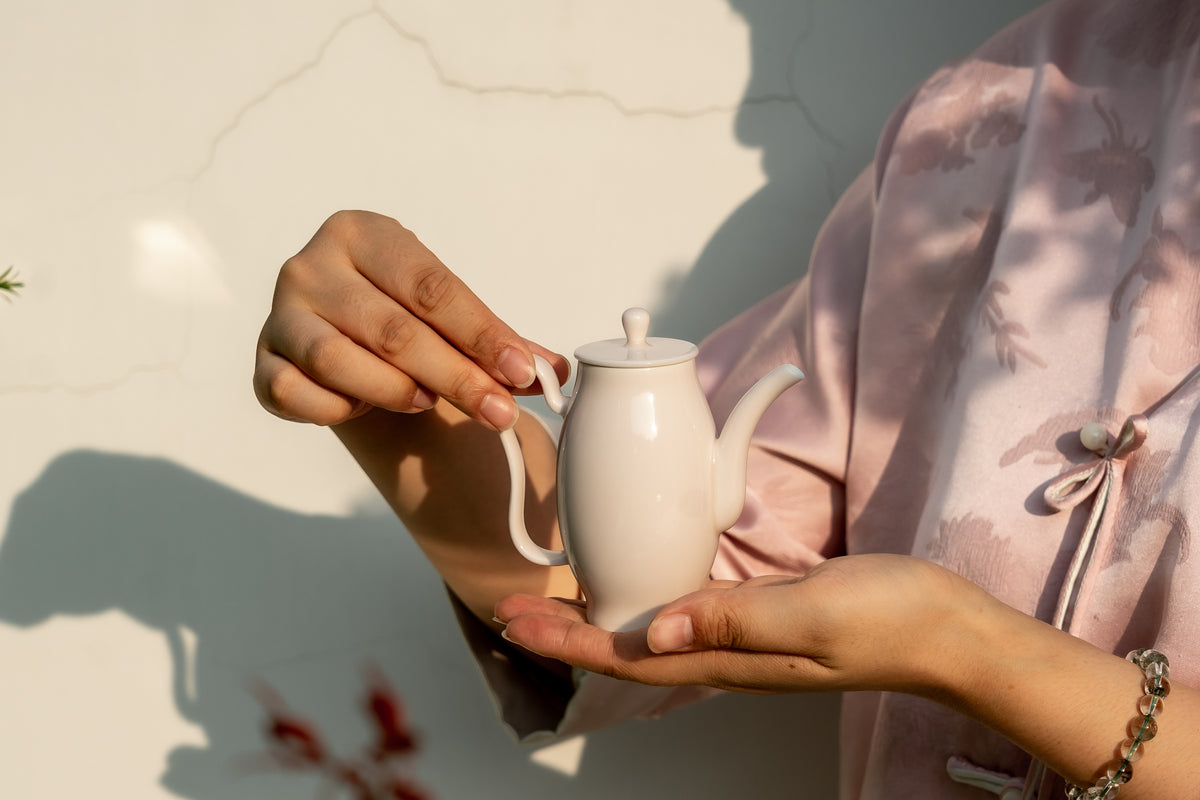Person holding a white teapot with sunlight casting shadows on a light background