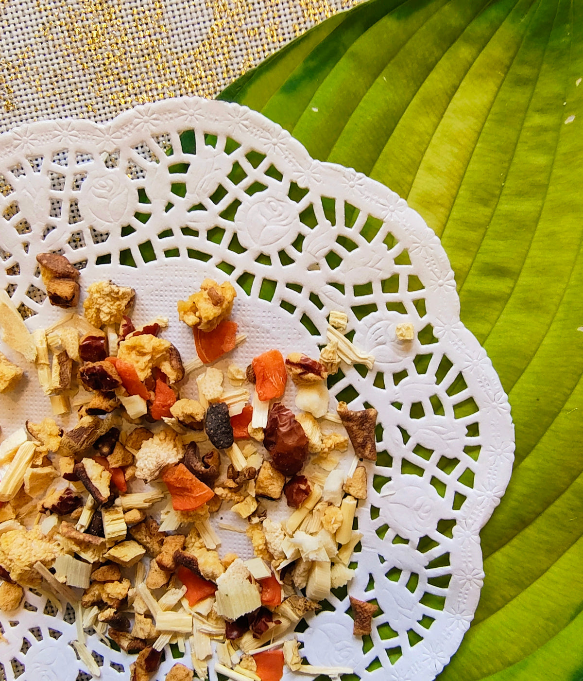 A close-up of a loose herbal tea blend presented on a white lace doily over a green leaf.