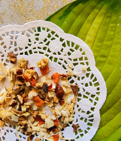A close-up of a loose herbal tea blend presented on a white lace doily over a green leaf.