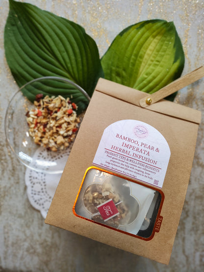 A kraft paper bag of Bamboo, Pear & Imperata Herbal Infusion tea with a clear window showing loose tea leaves, styled with two green leaves and a glass bowl of dried ingredients on a light textured background.