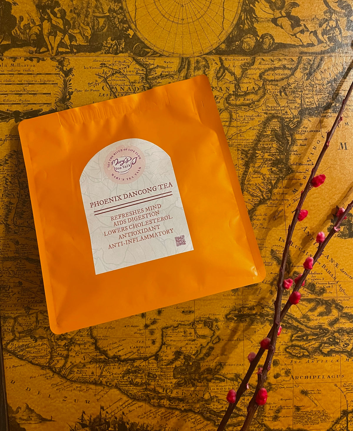 An orange stand-up pouch of Phoenix Dancong Tea with a white label, styled on a vintage map background with a cherry blossom branch.