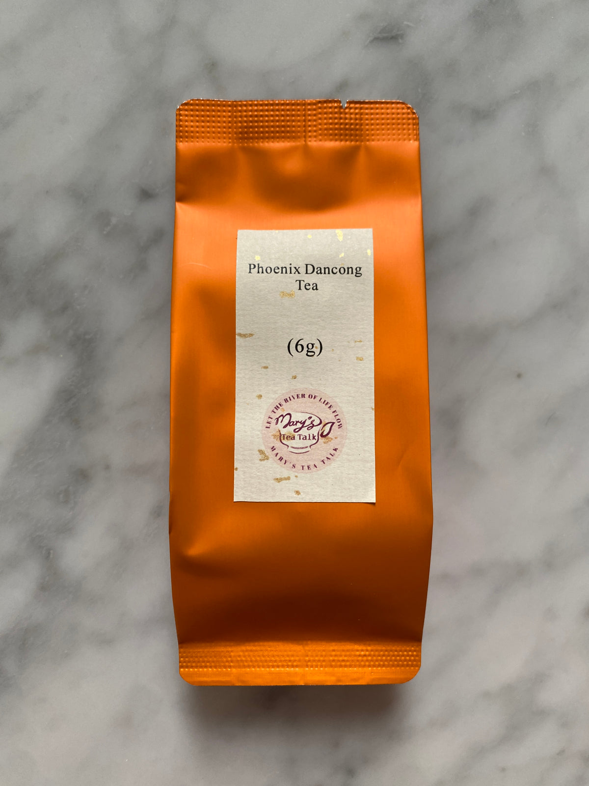 An orange foil packet of Phoenix Dancong Tea, 6g, with a cream label, placed on a gray marble surface.