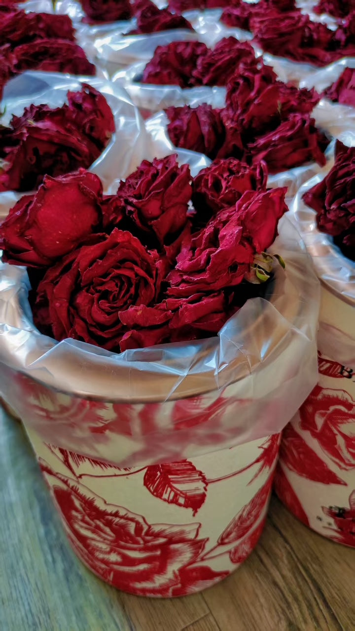 Red flowers in a decorative container with floral pattern on a wooden surface