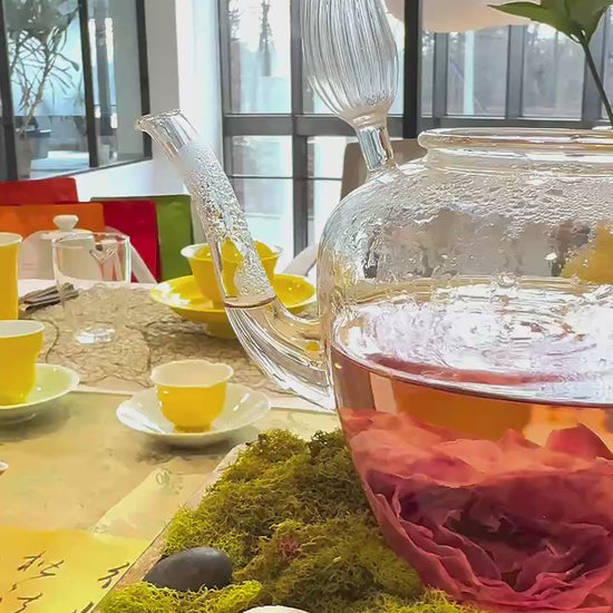 A large glass teapot with a rose bloom swirling in the water inside.