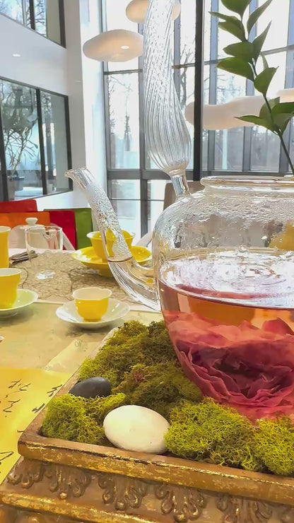 A large glass teapot with a rose bloom swirling in the water inside.